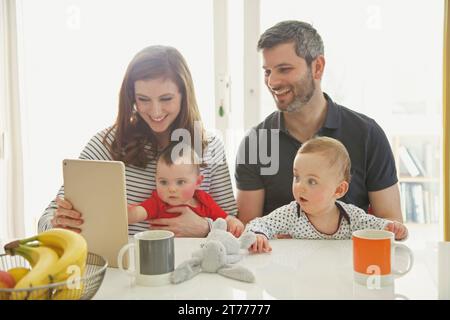 Couple Sitting at Table with Baby Twins Using Digital Tablet Stock Photo