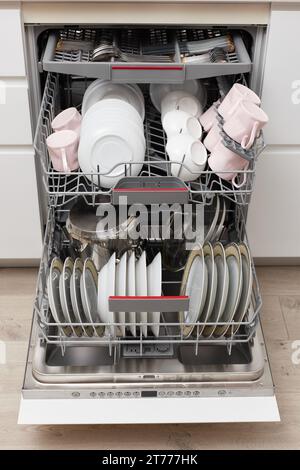 Open built-in dishwasher machine with clean cutlery, dishes, plates in white modern kitchen. front view Stock Photo