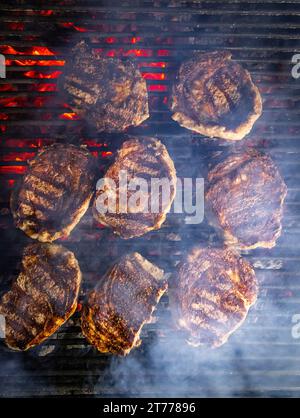 Steaks are generously covered in seasoning. Smoke is rising from the grill Stock Photo