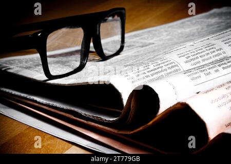 glasses on stack of newspapers on wood table Stock Photo