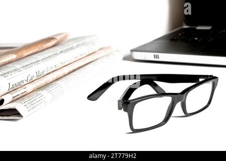 closeup glasses near financial newspaper in front of a unfocused notebook on white table Stock Photo
