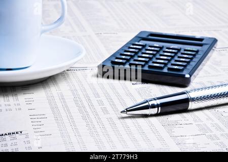detail of a pen near a calculator with cup of coffee on financial newspaper under light tint blue Stock Photo