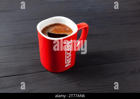 A red Nescafe cup of strong coffee on black table. Red mug with coffee Nescafe. Ukraine, Kharkiv - October 20, 2023 Stock Photo