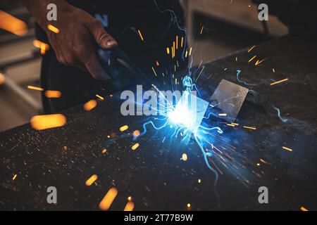 Male worker hand welding steel rack, close up. Sparks in metalworking. Stock Photo