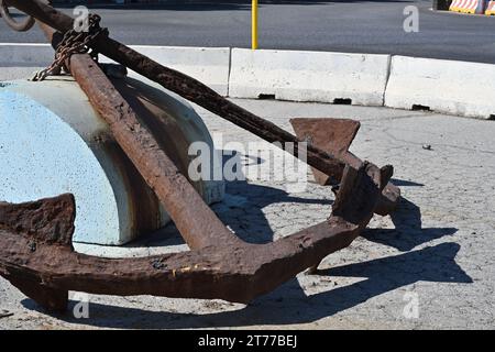 View on two old rusty anchors with chain placed in the middle of roundabout with traffic sign and concrete barrier. Stock Photo