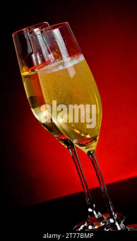 champagne flutes with golden bubbles on dark red light background with space for text Stock Photo