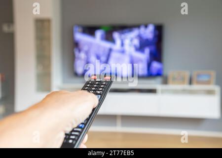 male hand holding tv remote control and watching tv in living room at home Stock Photo