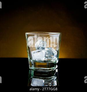 empty whiskey glass with ice and warm light on black table, with reflection Stock Photo