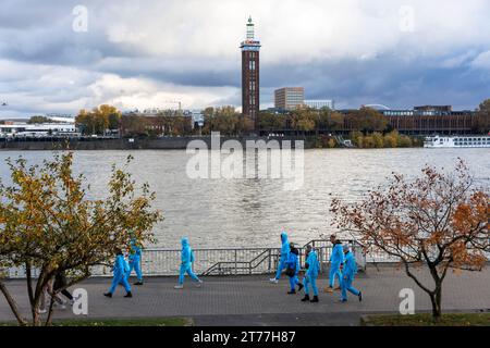 on the day of the opening of the carnival session on 11.11.23 a group of people in blue overalls walk along the banks of the Rhine, old tower of the f Stock Photo