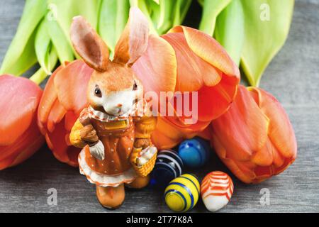 female Easter bunny with Easter eggs and tulips on gray background Stock Photo