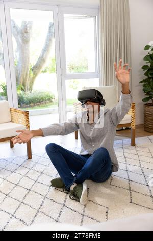 Biracial man using vr headset touching virtual screen at home Stock Photo