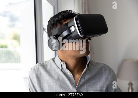 Biracial man using vr headset next to window at home Stock Photo