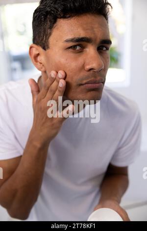 Biracial man applying face cream in bathroom at home Stock Photo