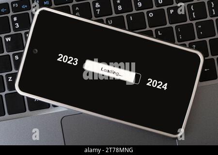 the concept of changing the year from 2023 to 2024. smartphone on the computer keyboard with the process of loading the new year. end of 2023 Stock Photo