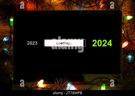 Office desk with 2024 loading bar on laptop screen on the background of a Christmas tree with bright lights at night. happy new year concept Stock Photo