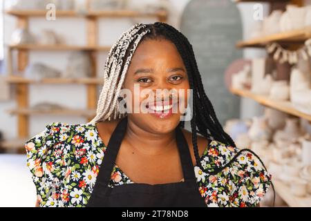 Happy african american female potter with braids, smiling in pottery studio Stock Photo