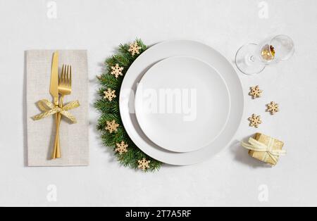 Christmas table setting with golden decorations and empty beige plate on a white background. New Year serving with empty plate for design. Top view, f Stock Photo
