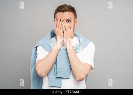 Man looks through fingers. Frightened middle aged guy covers face with hands. Creepy scary sight. Stock Photo