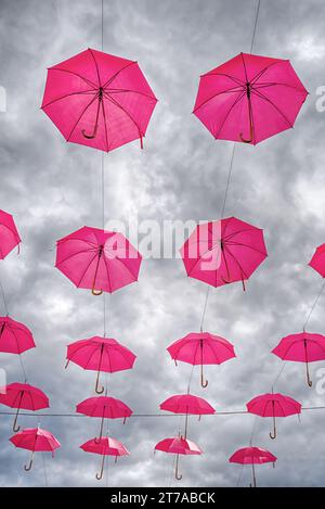 multiple pink open umbrellas hanging in the sky with a moody cloud background Stock Photo