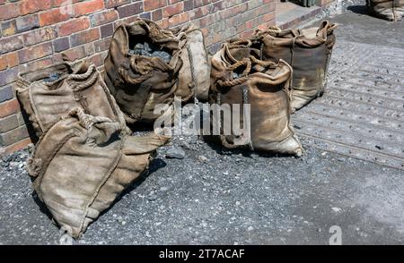 Heavy bags filled with coal resting against a brick wall in an urban environment on a sunny day Stock Photo