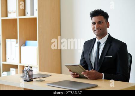 Portrait of cheerful Indian entrepreneur working on tablet computer at office desk Stock Photo