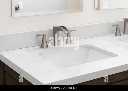 A bathroom faucet detail with a bronze widespread faucet, white marble countertop, and a dark wood cabinet. Stock Photo