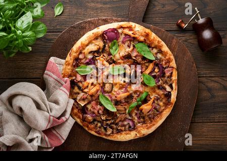Pizza. Traditional Bacon pizza with ham, mushrooms, pickled cucumber and cheese and cooking ingredients tomatoes basil on wooden table backgrounds. It Stock Photo