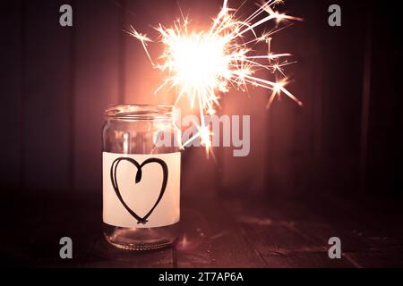 Hope for love, still life with glass jar with heart symbol and burning sparkler. Romantic pink tone. Background with copy space for Valentine. Stock Photo
