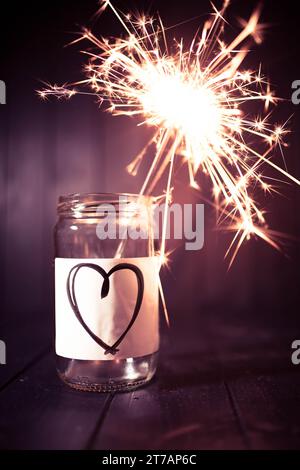 Hope for love, still life with glass jar with heart symbol and burning sparkler. Romantic pink tone. Background with copy space for Valentine. Vertica Stock Photo