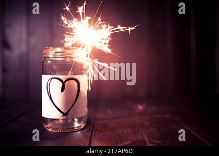 Hope for love, still life with glass jar with heart symbol and burning sparkler. Romantic pink tone. Background with copy space for Valentine. Stock Photo