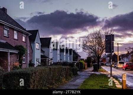Nightscape with an empty residential street lit by pale street lamps with white semi-detached houses. Road sign. Grass verge. Street. UK. Stock Photo