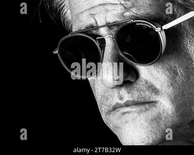 Black and white face close-up portrait of an elder charismatic man wearing round sunglasses Stock Photo