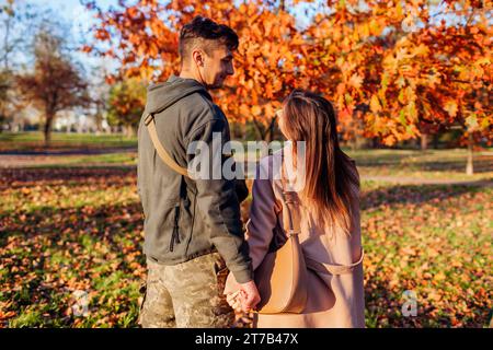 Back view of soldier in ukrainian uniform and his wife walking in autumn park. Couple hugging after long separation. Homecoming Stock Photo