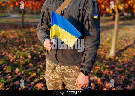 Close up of Ukrainian flag in soldier's hand. Defender wears military uniform with chevron outdoors. War in Ukraine. Man fights for freedom independen Stock Photo