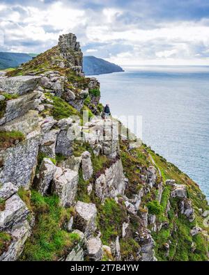 A hiker pauses on a rock ledge at the Valley of Rocks, near Lynton, north Devon, UK. Stock Photo