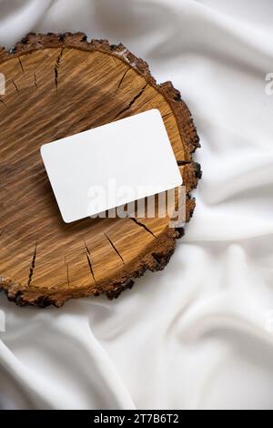 A wooden slice sits atop a bed of soft fabric, accompanied by a blank paper card, ideal for writing a message or sending a special note Stock Photo
