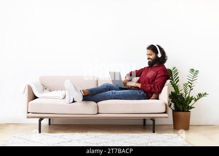 Guy reclining on couch at home, watching movie on laptop Stock Photo