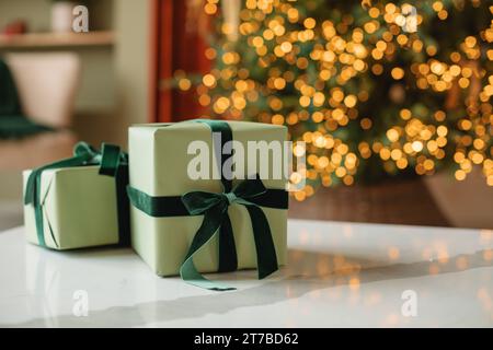 Stack of wrapped Christmas gifts in front of an illuminated Christmas tree in a living room Stock Photo