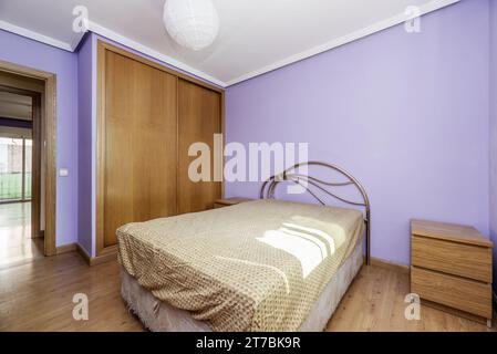 A room in an apartment with a built-in wardrobe with sliding oak doors with a double bed with a metal headboard Stock Photo