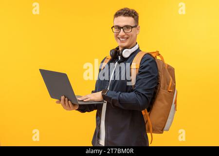 Happy young man student using laptop on yellow background Stock Photo