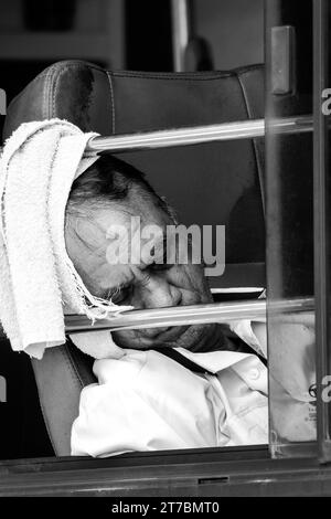 Black and white street portrait of an Indian bus driver having a nap in his bus. Stock Photo