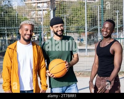 Portrait of three diverse young men lookingsmiling at camera on a basketball court with a ball in their hand  Stock Photo