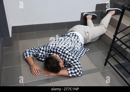 Unconscious man lying on floor after falling down stairs indoors Stock Photo