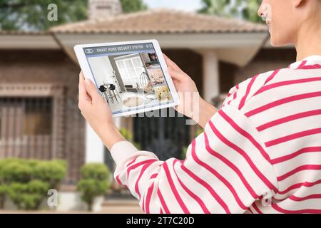 Woman using smart home security system on tablet computer near house outdoors, closeup. Device showing different rooms through cameras Stock Photo