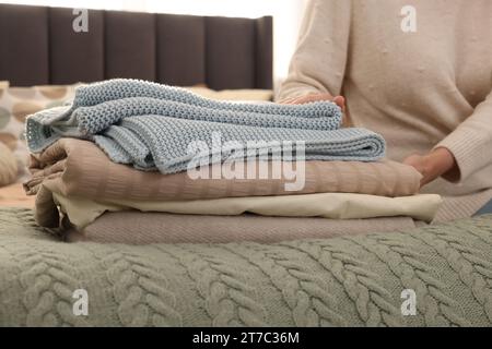 Woman with stack of different folded blankets on bed, closeup. Home textile Stock Photo