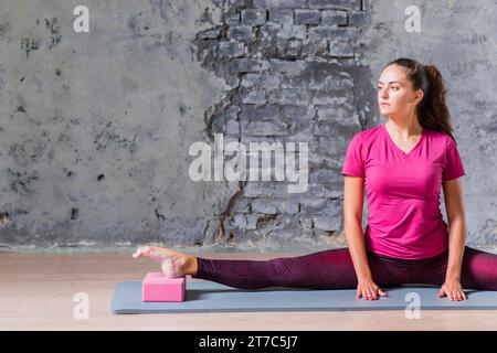Young woman practicing advanced yoga using pink block against grey wall Stock Photo