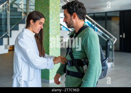 Mechanical exoskeleton, female physiotherapist doctor putting tapes on disabled person with robotic skeleton, physiotherapy in a modern hospital Stock Photo