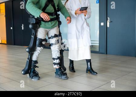 Mechanical exoskeleton, female doctor physiotherapist with unrecognizable disabled person with robotic skeleton in rehabilitation, physiotherapy in a Stock Photo