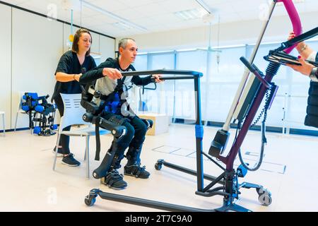 Mechanical exoskeleton. Female physiotherapy medical assistant lifting disabled person with robotic skeleton. Futuristic rehabilitation Stock Photo