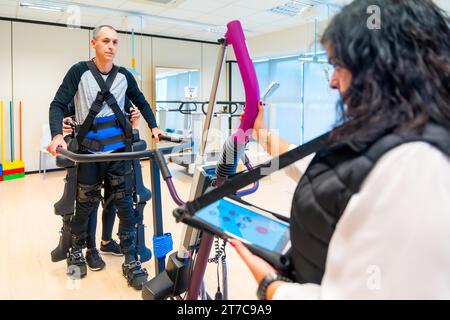 Mechanical exoskeleton. Female physiotherapy medical assistant with disabled person lifted with robotic skeleton. Futuristic rehabilitation Stock Photo